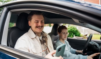 Kaksi iloista ihmistä autossa käyttämässä pysäköintijärjestelmää etänä puhelimella